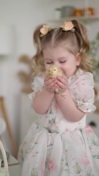 明るい青い目と花のピンで装飾された豪華なカールの少女は わずかな笑顔で優しく見て黄色い鶏を保持しています — ストック動画