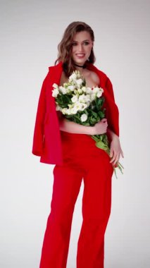 Dalgalı saçlı şık bir kadın parlak kırmızı bir takım elbiseyle cazibe saçar. Zarif bir buket beyaz çiçekle tamamlanır.