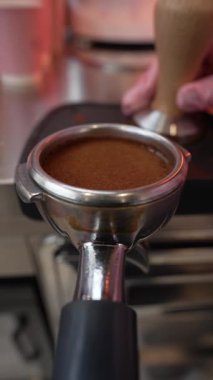 Bir kahveci, bir şehir kafesinin tezgahındaki portafiltere taze espresso döker. Sabah kahve ritüeli, profesyonel ekipman..