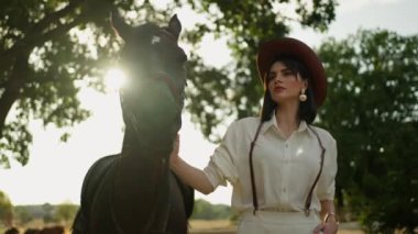 Şapkalı genç bir kadın atıyla yürüyor. Yaz güneşli bir akşam.