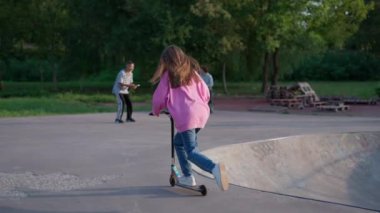 Küçük kız kaykay parkında scooter sürmeyi öğreniyor.