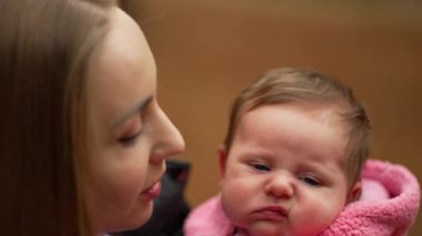 Anne şefkatle bebeğinin yanağını öper, bebek rahat pembe postu sarar, anne sevgisinin resmi ve sonbahar arkaplanına karşı koruma..