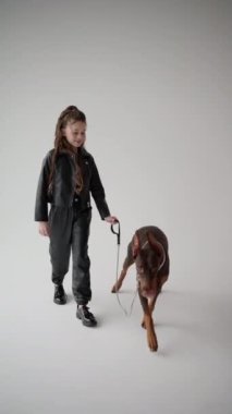 Siyah elbiseli kız beyaz arka planda Doberman 'ı tasmalı tutuyor..