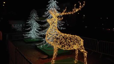 Altın ren geyiğinin parlak ışık heykeli Noel pazarındaki neşeli peri ışıklarının zemininde parlıyor