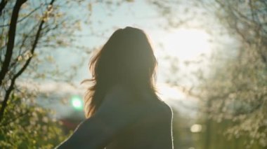 Bardaklı kadın bahar bahçesinde duruyor, batan güneşle aydınlanıyor. Kolları açık ve saçları rüzgarda savruluyor, doğada özgürlük ve neşe hissi yaratıyor..