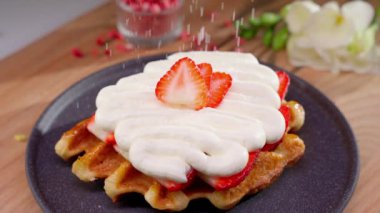 Kalın tereyağlı kremayla kaplı iştah açıcı waffle 'lar ve siyah tabakta taze çilek dilimleri. Tatlı çok lezzetli ve çekici görünüyor..