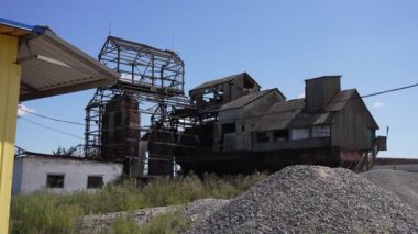 Eski metal yapıları ve yıkık duvarları olan terk edilmiş sanayi binası. Endüstriyel bozulmanın kasvetli atmosferi berrak mavi gökyüzü altında.