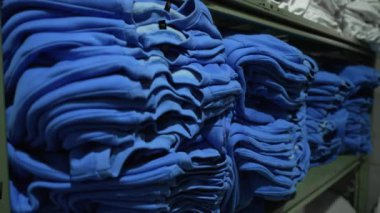 Depodaki raflarda düzgünce katlanmış çok sayıda mavi eşofman üstü var. Sweatshirt 'ler sıralanır, tekstil üretiminde düzen ve düzen sağlanır..