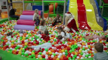 Noel Baba oyun alanındaki çocukları ziyaret ediyor. Noel Baba neşeli çocuklarla çevrili renkli top havuzunda kapalı sahada.