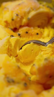 Kaşıkla mango kepçeleme dondurması. Zengin sarı renk ve kremalı dondurmanın mango parçacıkları iştah açıcı bir görünüm yaratır.