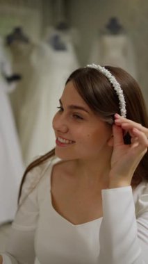 Gülümseyen gelin gelinlik salonunda inci madalyalı alyansı deniyor. Mutlu ve heyecanlı görünüyor. Özel gününe hazırlanıyor..