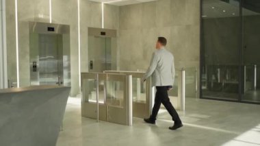 Gri takım elbiseli işadamı, güncel ofis lobisinde turnikelerin önünden geçiyor..