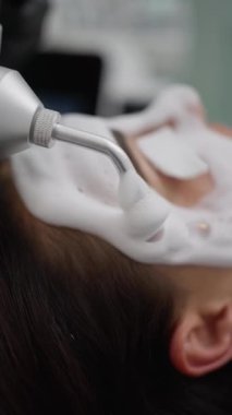 Güzellik salonundaki yüz temizleme prosedürüne yakın çekim. Güzellik uzmanı hastaların yüzüne köpük sürmek için özel bir cihaz kullanıyor..