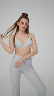Kendine güvenen manken, eski güneş gözlüğü ve boğucuyla tamamlanmış modern gümüş renkli bluz ve parlak pantolonu sergiliyor..