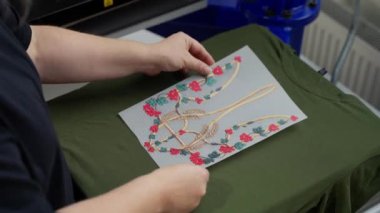 Sanatçı geleneksel Ukrayna süsünü yeşil tişörte basıyor. Eller, uygulamadan önce dokunun üzerine dikkatlice desen yerleştir.