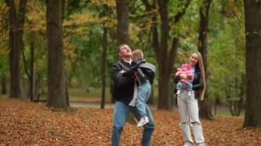Sonbahar parkında yürüyüş yaparken genç bir aile. Baba oğlunu kaldırır, onunla oynar ve anne bebeği gülümseyerek kucağına alır..