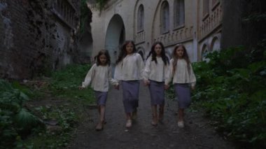 Vintage kostümlü çocuklar el ele tutuşup eski binanın yıkıntılarının yanında yürüyorlar. Sahne, geçmişle bağlantıyı vurgulayarak tarihi miras ve gizemli bir atmosfer yaratıyor..