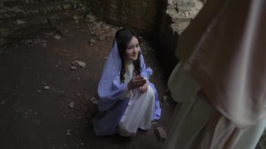 Ortaçağ kostümü giymiş, taştan valsle karanlık odada dikilen kız, yardım için başka bir figüre uzanıyor..