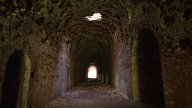 Tavandaki deliklerden geçen kemerli kemerli tuğla tünel ışığın nüfuz ettiği. Tünel zaman ve yıkım belirtileri gösteriyor, yere saçılmış taşlar var..