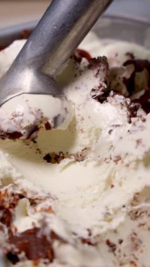 Bir kepçe çikolata parçalı vanilyalı dondurma metal kaşıkla alınıyor. Dondurma iştah açıcı ve taze görünüyor. Kremalı taban ve kıtır kıtır çikolata..