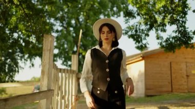 Kaliteli, esinlenmiş elbiseli genç bir kadın ahşap çitin yanında güvenle yürüyor ve zarafet gösteriyor..