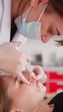 Cerrahi maskeli bir estetikçinin klinikteki rahat bir kadına yüz tedavisi uygularken yakın plan görüntüsü..