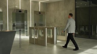 Ofis asansörlerine yaklaşan işadamı modern ofis lobisinden ışıklı lobiye doğru adım atıyor..