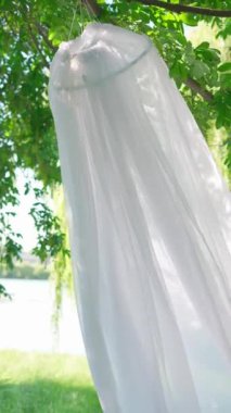 Güzelce örtülmüş beyaz gölgelik ağaçtan sarkan, sakin ormanda yemyeşil yaprakların üzerine kurulmuş..