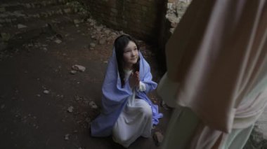 Genç bir kızın canlandırıcı bir sahnesi. Beyaz ve mavi bir elbise giymişti. Diz çökmüş ve umutlu bir ifadeyle yukarı bakıyordu..