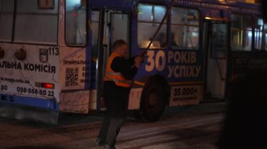 Yansıtıcı yelek giyen bir belediye çalışanı gece tramvay kablolarını tamir ederken görülüyor..