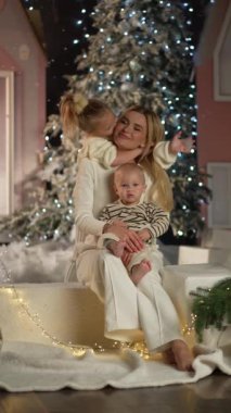 Güzel dekore edilmiş bir Noel ağacının önünde iki çocuğuyla oturan bir annenin yürek ısıtan bir sahnesi..