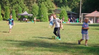 Bu canlı görüntü, parkta çimenli bir alanda futbol oynayan bir grup çocuğu gösteriyor..