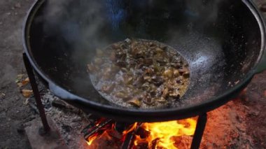 Bu görüntü, mantarların açık bir ateş üzerinde büyük bir tavada cızırdamasını gösteriyor..