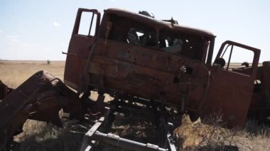 Eski, paslı bir kamyon açık bir arazide terk edilmiş, parçalanmış ve zamanla yıpranmış olarak duruyor..