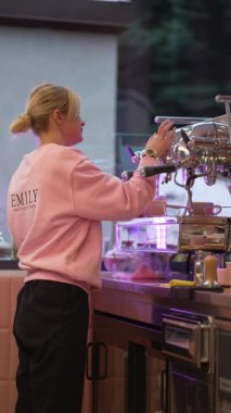 Pembe kazaklı bir barista kahve makinesinde çalışıyor, kahve içeceği yapmaya odaklanmış..