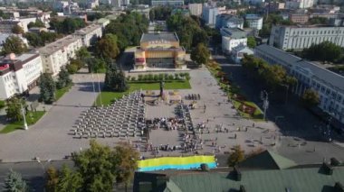 Merkezi bir anıtın etrafında toplanan insanlarla dolu bir şehir meydanının havadan görünüşü.