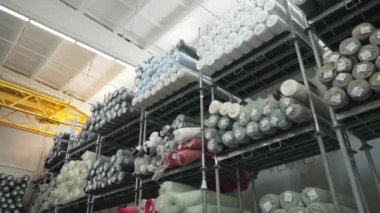 Tekstil imalatında malzeme depolama sırasında geniş bir depodaki yüksek endüstriyel raflarda büyük rulo kumaşlar düzenli olarak depolanır..