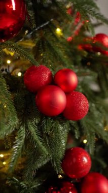 Parlak kırmızı süslemelerle süslenmiş Noel ağacının yakın görüntüsü, pırıl pırıl mücevherler ve yemyeşil dallar arasında parıldayan yumuşak ışıklar.