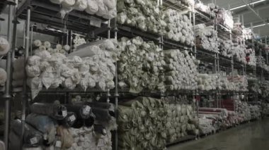 Metal raflarda yığılmış çeşitli malzeme ve renklerin bulunduğu büyük bir sanayi deposu..