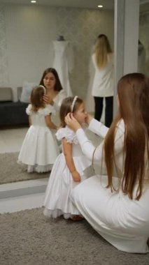 Bir kadın beyaz bir elbise giyen genç bir kıza tacını takar. Bu sırada aynanın önünde iyi aydınlatılmış bir odada aynanın karşısına geçer. Yansımalar etkileşimlerini yansıtırken hassas ve zarif bir an yaratır..