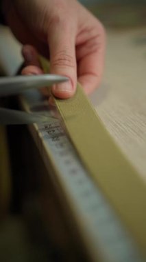 Yakın plan bir el, yeşil kumaştan bir şeridi masa üzerinde mezura ile dikkatlice ölçüyor..