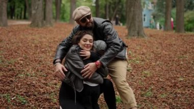 Üç insanın sonbahar yapraklarıyla çevrili bir parkta sıcacık kucaklaştığı sevgi dolu bir aile anı..