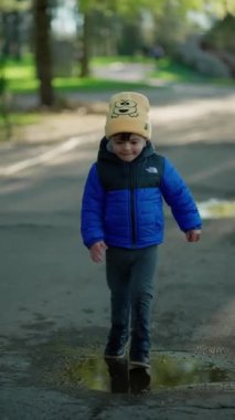 Sarı şapkalı ve mavi ceketli genç güneşli bir günde su birikintileriyle yolda yürüyor..