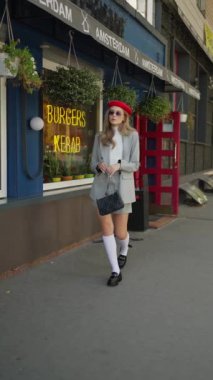 Genç bir kadın, kırmızı bereli ve klasik gri takım elbiseli ve diz hizasında kafenin önünden güvenle geçer..