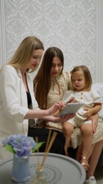 Anne ve çocuk danışman ile alışveriş yaparken kanepede oturuyorlar, gülümsüyorlar, rahat ve zarif bir ortamda tablete bakıyorlar..