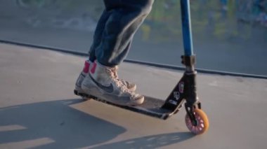 Scooter güvertesinde, spor ayakkabısı giymiş, pürüzsüz bir kaykay parkı yüzeyinde insanların ayaklarının yakın görüntüsü..