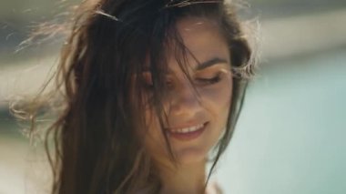 Suyun yanında rüzgarda hafifçe esen saçlarıyla gülümseyen bir kadının sakin bir yakın çekimi..
