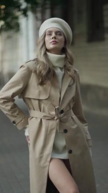 Bej yağmurluk, beyaz balıkçı yaka ve bereli şık bir kadın sokakta poz veriyor..