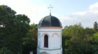 Kubbeli çatısı ve tepesinde yemyeşil ağaçlarla çevrili haçı olan tarihi kilise çan kulesinin manzarası..