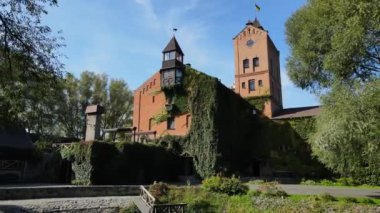 Yeşil sarmaşıklarla kaplı tarihi bir tuğla bina, kuleleri var ve yemyeşil ile çevrili..